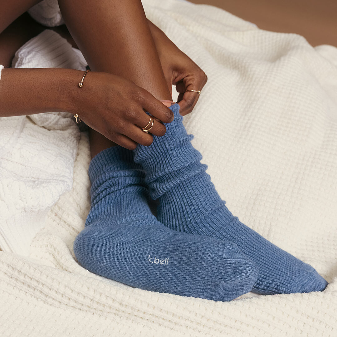 Person wearing blue socks with 'k. bell' branding on a white textured surface
