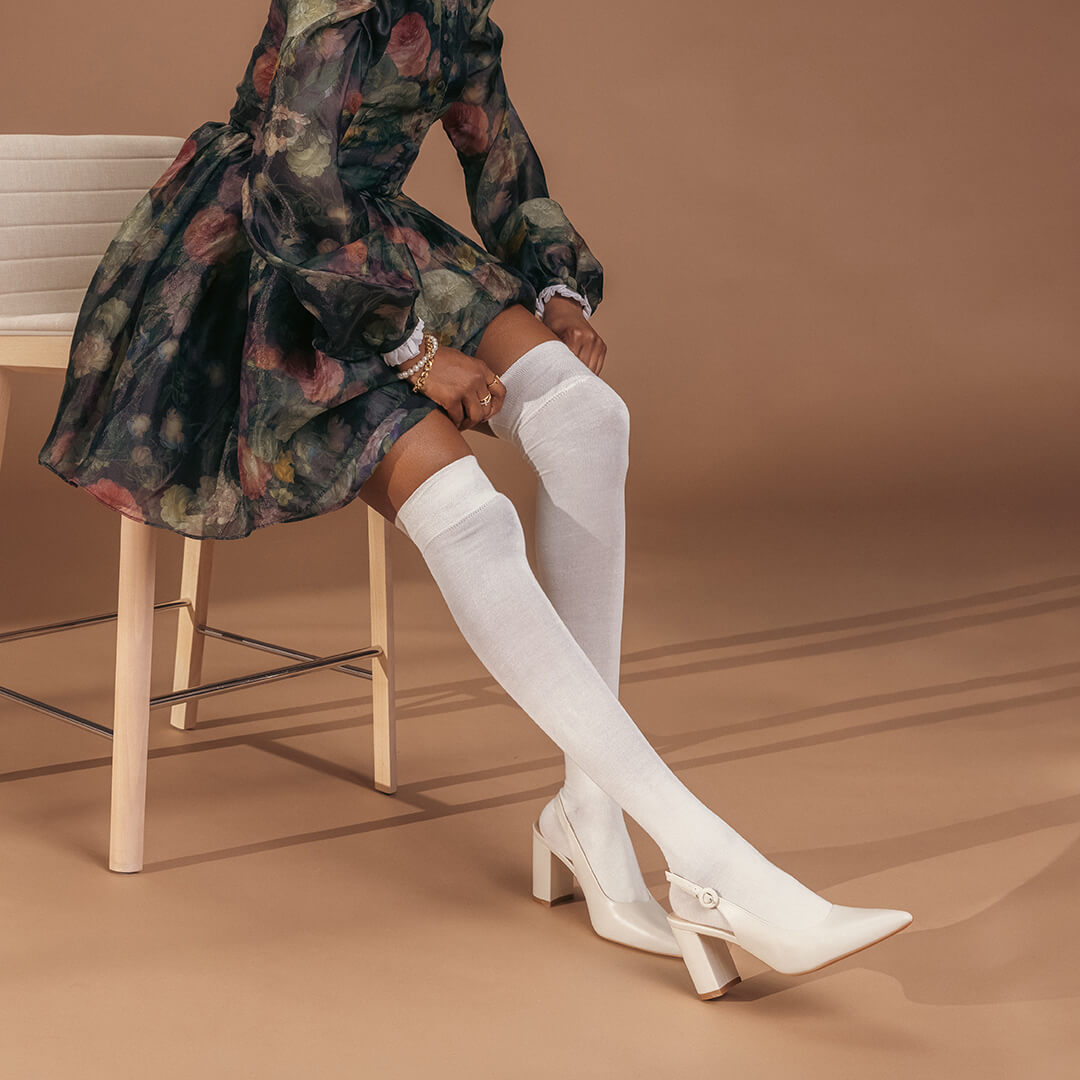 Person wearing a floral dress and white thigh-high socks on a brown background