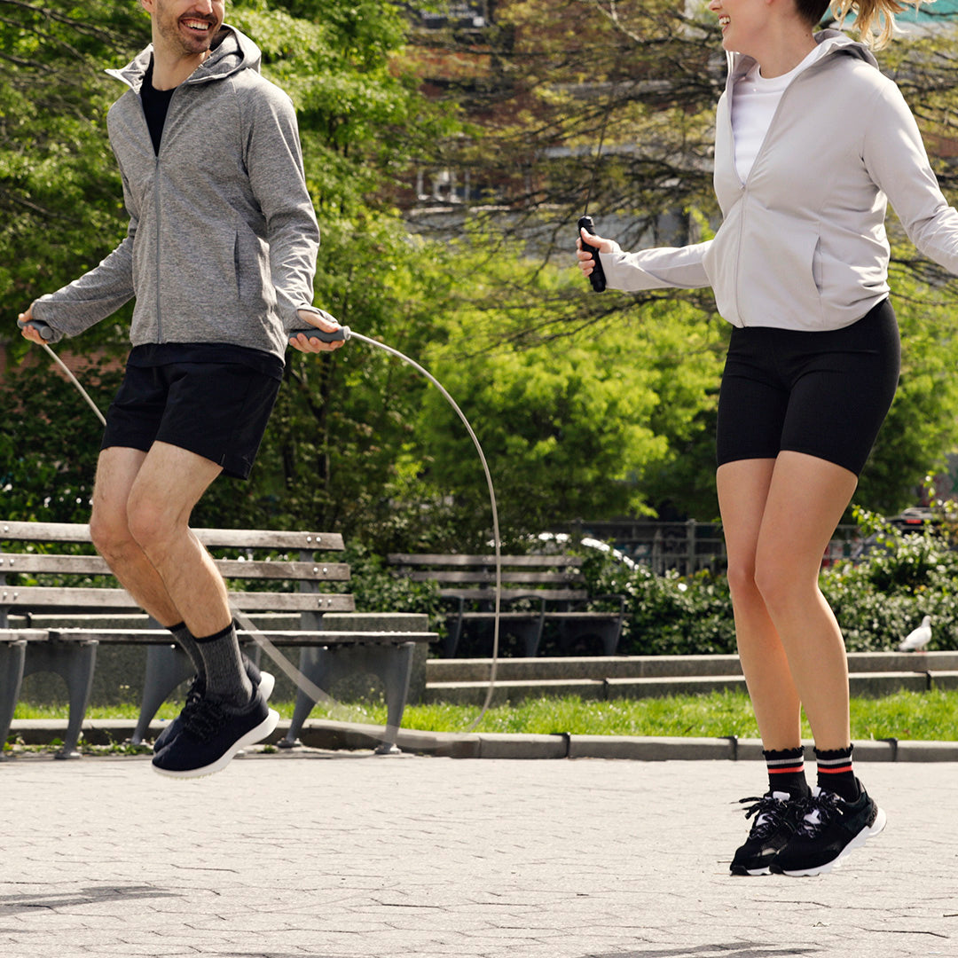 Two people jumping rope in a park with trees and benches in the background.