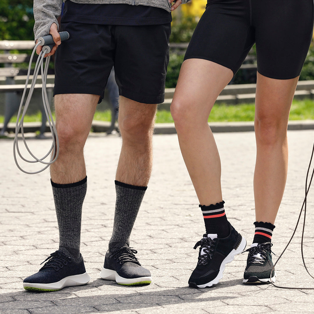 Two people wearing black athletic shoes and socks on a paved path.