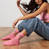 Woman wearing pink socks with the phrase "Women Unite," sitting on a wooden floor.