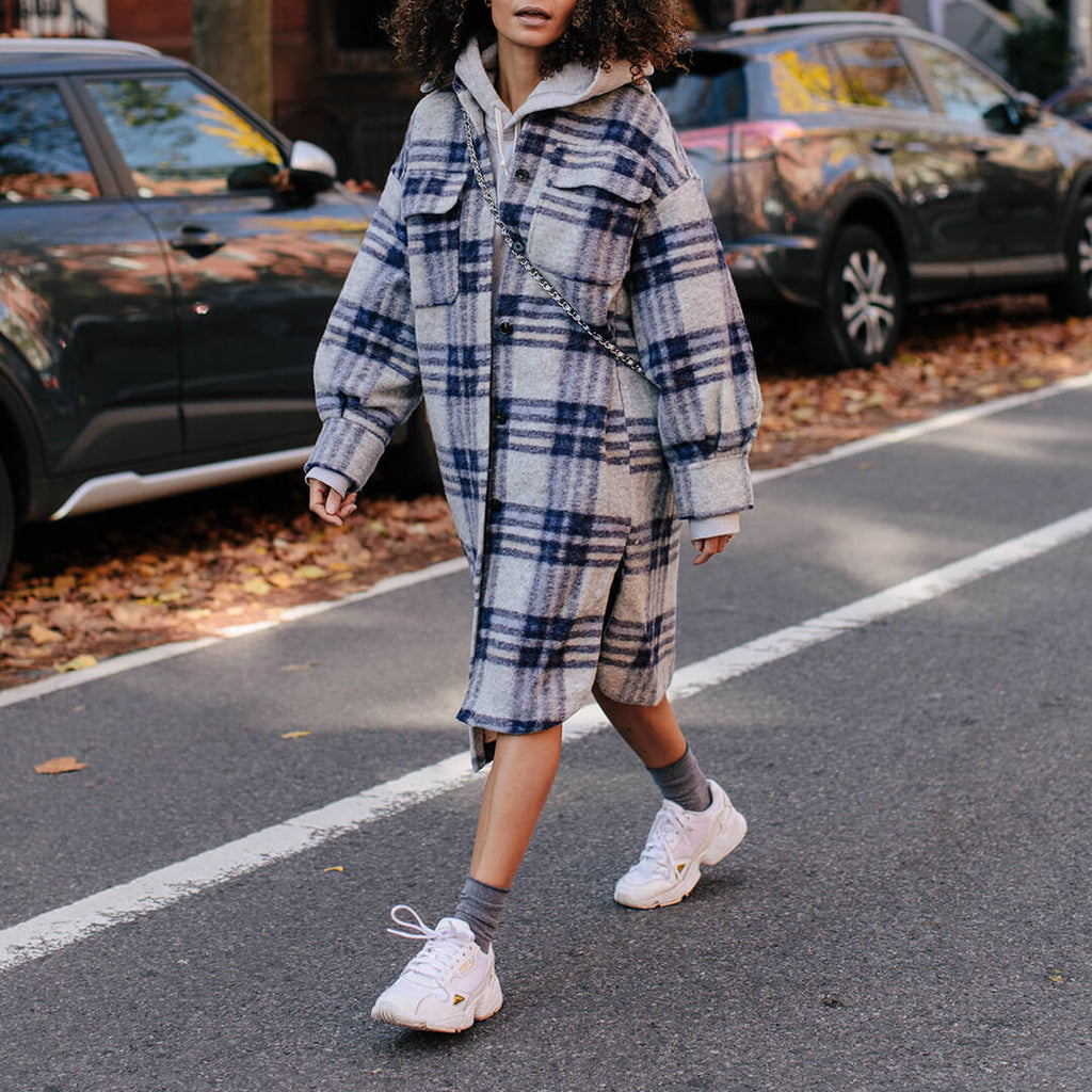 Person wearing a plaid outfit with white sneakers and gray roll top socks on a street.