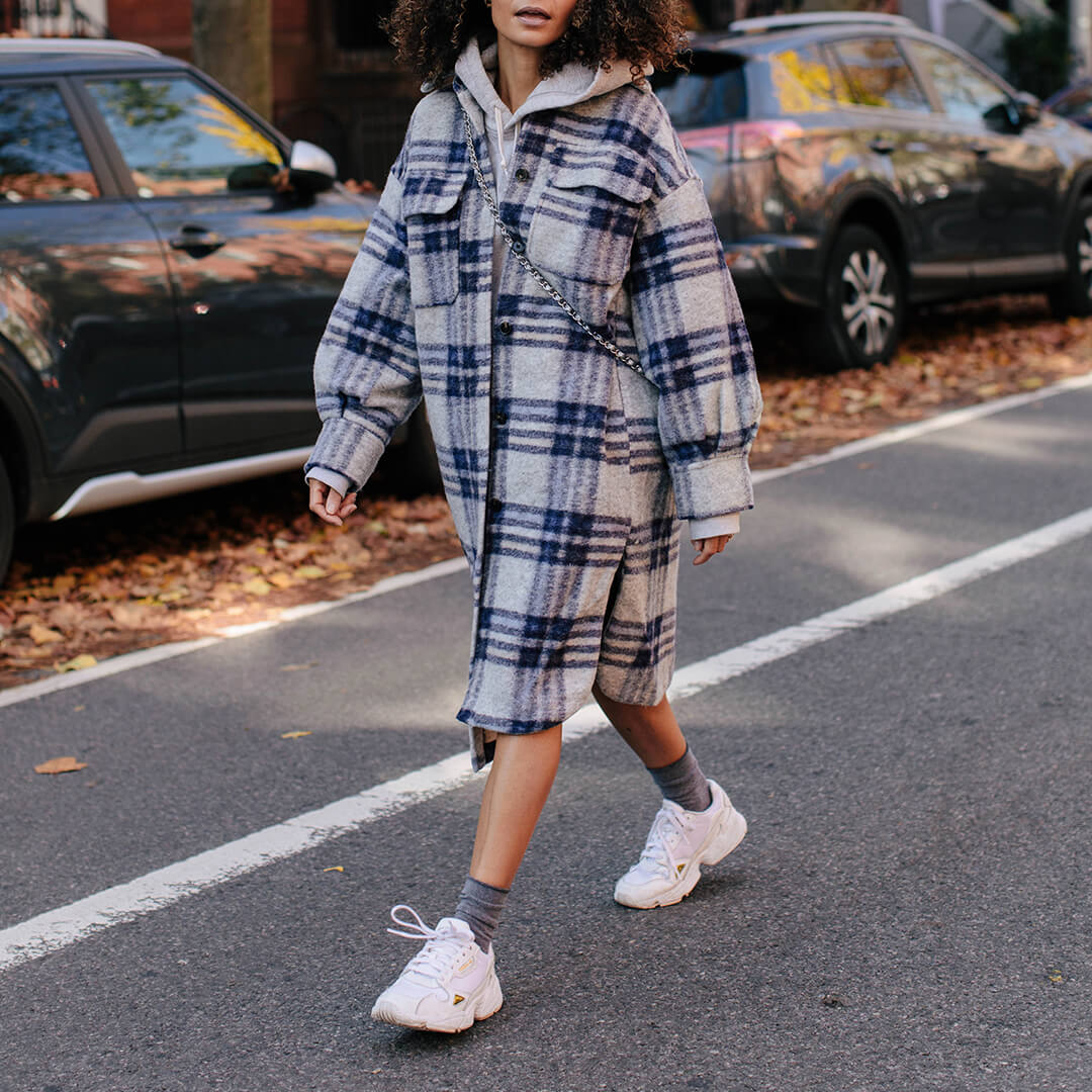 Person wearing a plaid outfit with white sneakers and gray roll top socks on a street.