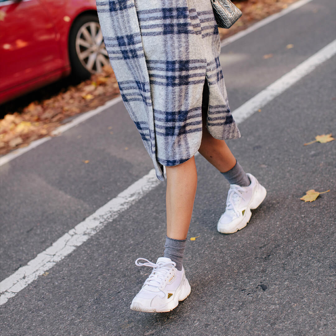 Person wearing a plaid outfit with white sneakers and gray roll top socks on a road.