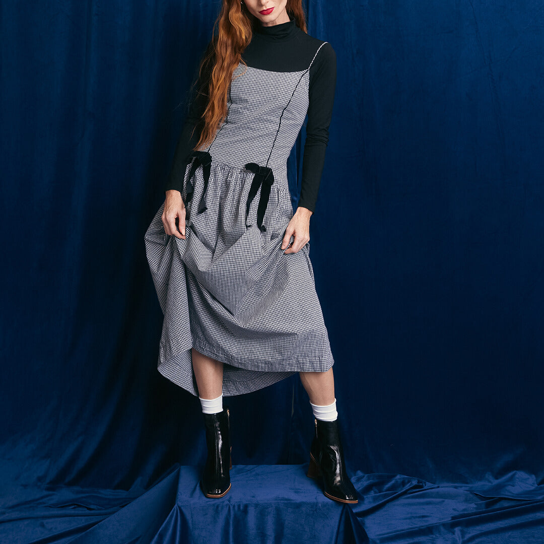 Person wearing a gray checkered dress with black accents against a blue backdrop
