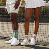 Two people standing on a tennis court and visible legs wearing tennis attire and crochet net socks. thumbnail
