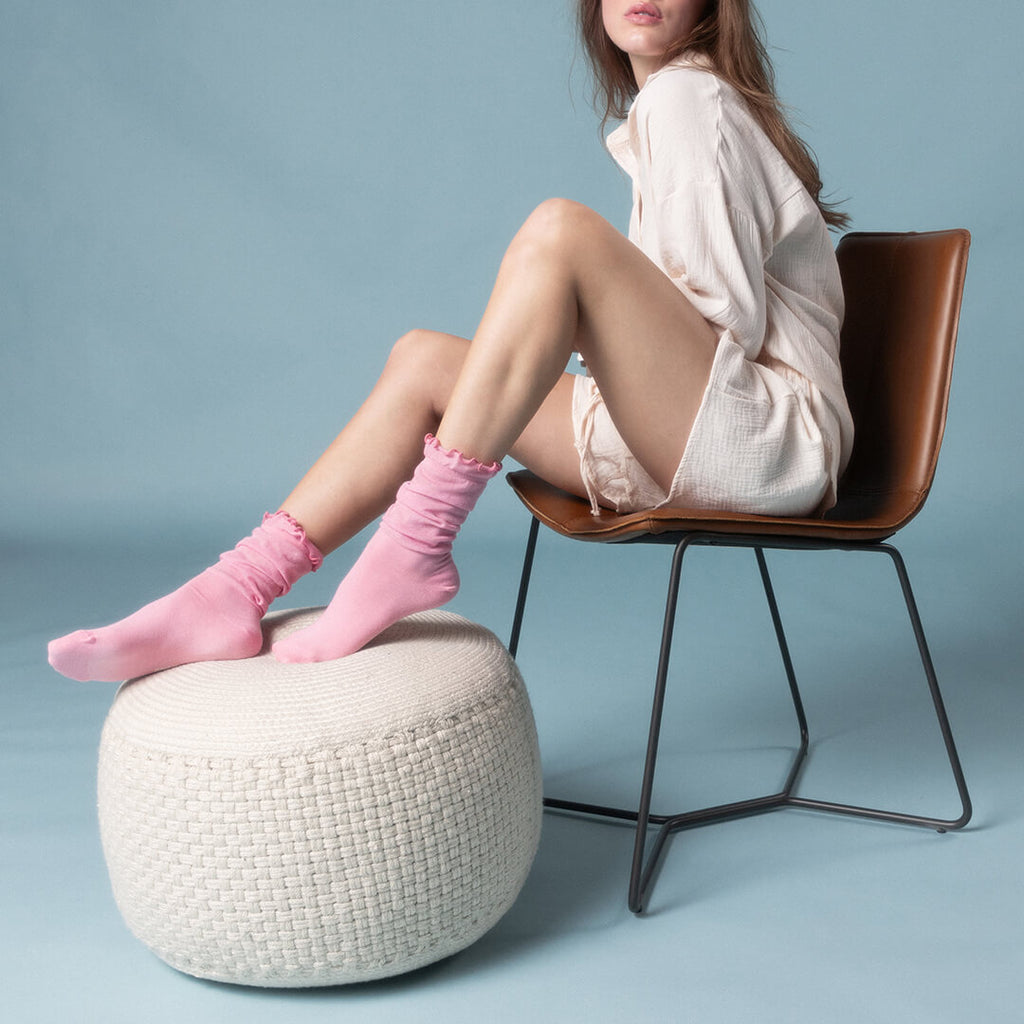 Woman sitting on a chair with pink sheer slouch socks on a light blue background