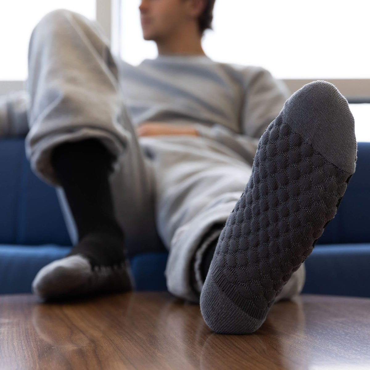 Person wearing gray socks sitting on a couch with feet up on a wooden table.