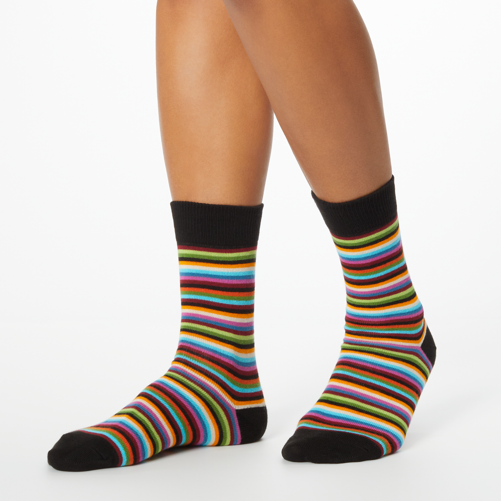 Profile view of a pair of women's HOTSOX crew socks with multicolor horizontal stripes worn by a woman
